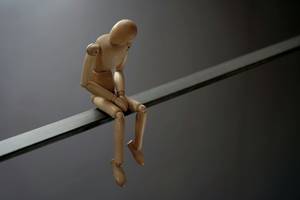 Quelle: Marco Bianchetti/Unsplash Holzfigur sitzt mit gesenktem Kopf und verschränkten Händen auf einer Kante